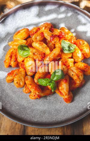 Nahaufnahme der italienischen Kartoffel Gnocchi mit Tomatensoße und frischem Basilikum auf grauer Platte auf Holzhintergrund. Stockfoto