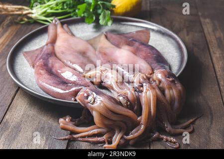 Rohe Kalmare auf grauen Platten mit Koriander und Zitronen. Auf dunklem Holzhintergrund. Stockfoto