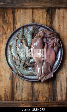 Rohe Meeresfrüchte. Frische Garnelen und Tintenfische auf grauem Teller. Holzhintergrund. Stockfoto