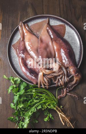 Rohe Kalmare auf grauen Platten mit Koriander und Zitronen. Auf dunklem Holzhintergrund. Draufsicht Stockfoto