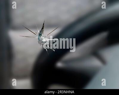 Nahaufnahme eines Steinstücks in der Windschutzscheibe eines Autos, Detailaufnahme von Rissen in Autoglas auf der Fahrerseite Stockfoto