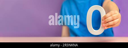 Nummer 0 in der Hand. Hand mit weißer Nummer Null über grünem Gras und lila Hintergrund, Konzept von Null-Emission CO2, Zinssätze, Nullpunktzahl in Stockfoto