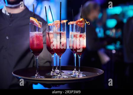 Der Kellner hält mehrere Gläser Champagner-Cocktails mit Grapefruitscheiben auf den Gläsern Stockfoto