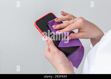 Nahaufnahme Frau Hände reinigen den Smartphone Bildschirm mit einem Fasertuch von Schmutz Staub und Virus. Reinigungs- und Desinfektionskonzept Stockfoto
