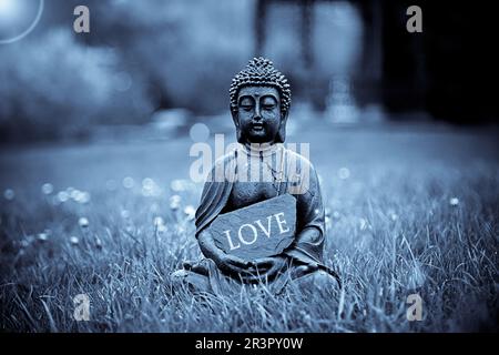 Buddha-Statue auf einer Wiese mit einem Schild mit der Aufschrift "Love" Stockfoto