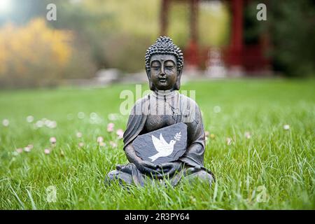 Buddha-Statue auf einer Wiese mit einer Friedentaube Stockfoto