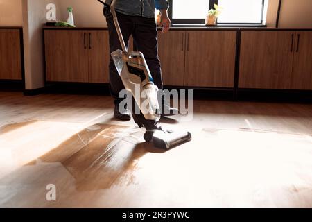 Mann saugt Holzfußboden im Loft-Raum mit Staubsauger. Schließen Stockfoto