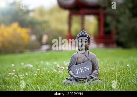 Buddha-Statue auf einer Wiese mit einem Schild MIT der Aufschrift ZEN Stockfoto