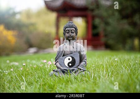 Buddha-Statue auf einer Wiese mit dem ying-Yang-Symbol Taijitu Stockfoto