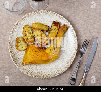 Gebratenes Hähnchen am Schenkel mit Knoblauch in eigenem Saft gewürzt und garniert mit Stücken gebackener Kartoffeln Stockfoto