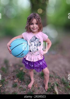 Hintergrund in Kristall-ähnlichem Unschärfeeffekt. Vorne hält ein Mädchen einen Basketball, während es für die Kamera posiert (NC State, April 2023) Stockfoto