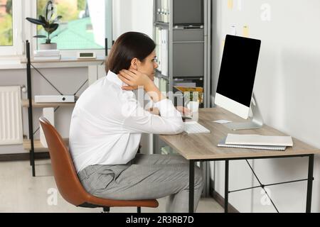 Junge Frau mit schlechter Körperhaltung, die im Büro am Arbeitsplatz sitzt. Das Symptom der Skoliose Stockfoto