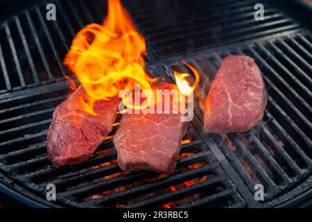Grillen Sie trocken gereiftetes angus-Sirloin-Beefsteak, das als Nahaufnahme auf einem Holzkohlegrill mit Feuer und Rauch gegrillt wird Stockfoto