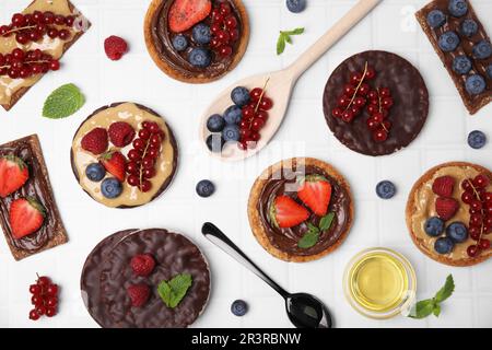 Frisches Roggen-Knusperbrot, knusprige Reiskuchen und Zwieback mit verschiedenen Belägen auf einem weißen Tisch, flach liegend Stockfoto