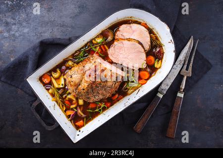 Traditioneller deutscher Schweinebraten, serviert mit Gemüse und Kräutern in dunkler Biersauce, serviert als Draufsicht in einer rustikalen Schmorpfanne Stockfoto