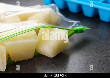 Gefrorene Blumenkohlpüree-Würfel in Plastikbeutel auf grauem Tisch, Nahaufnahme Stockfoto