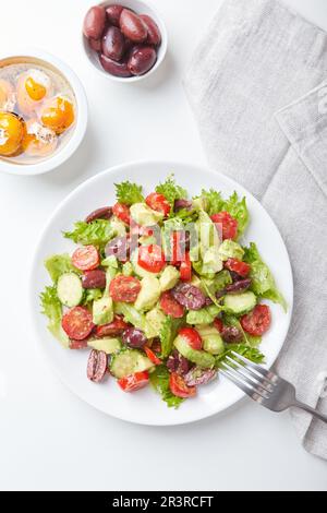 Salat mit Salat, Gurken, Tomaten, Oliven und Avocados in weißem Teller auf dem Tisch Stockfoto