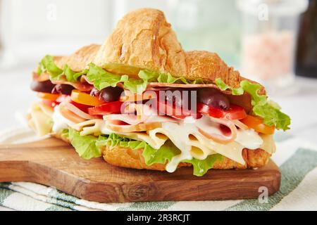 Croissant Sandwich mit Käse, Schinken, Salat, Tomaten, Oliven und köstlicher Sauce auf Holzbrett. Stockfoto