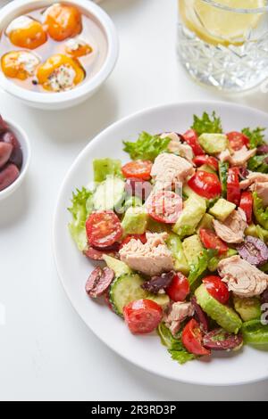 Salat mit Thunfisch, Salat, Gurken, Tomaten, Oliven und Avocados in weißem Teller auf dem Tisch Stockfoto