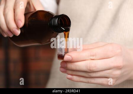 Frau, die Sirup aus der Flasche in den Messbecher gießt, Nahaufnahme. Erkältungsmedizin Stockfoto