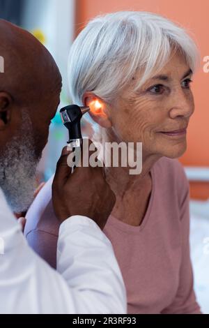 Vertikale eines vielschichtigen Oberarztes mit Otoskop am Ohr einer älteren Patientin, Kopierraum Stockfoto