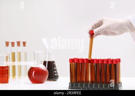 Wissenschaftler, der das Reagenzglas mit brauner Flüssigkeit in den Ständer auf dem weißen Tisch legt, Nahaufnahme Stockfoto