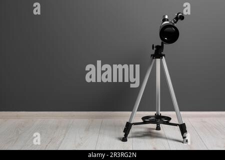 Stativ mit modernem Teleskop nahe der grauen Wand. Platz für Text Stockfoto