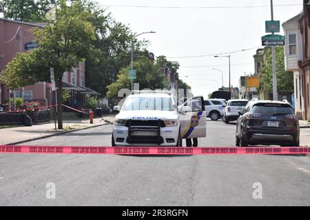 Polizeibeamte vom Philadelphia Police Department haben Tatortband aufgehängt und den Tatort gesichert. Zwei Menschen erschossen, eine Person wurde am 24. Mai 2023 bei einer Schießerei am helllichten Tag in Philadelphia, Pennsylvania, USA, für tot erklärt. Um 2:51 Uhr Eastern Time, Mittwochnachmittag an der Kreuzung West Susquehanna Avenue und North Gratz Street, wurde ein 31-jähriger schwarzer Mann einmal in den linken Arm geschossen, Einmal auf der linken Seite und einmal auf dem Rücken und wurde mit einem privaten Auto ins Krankenhaus transportiert, wurde er später für tot erklärt. Das zweite Opfer, ein 28-jähriger Schwarzer Stockfoto