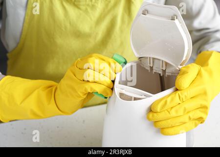 Frau in gelben Handschuhen, die elektrischen Wasserkocher auf einem weißen Tisch reinigt Stockfoto
