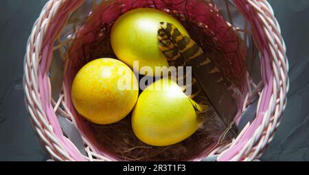 Farbenfroh bemalte, glänzende Ostereier aus Marmor in einem Korb mit zarten Federn aus der Nahaufnahme. Nest mit Stroh - Osterdekoration auf der Stockfoto