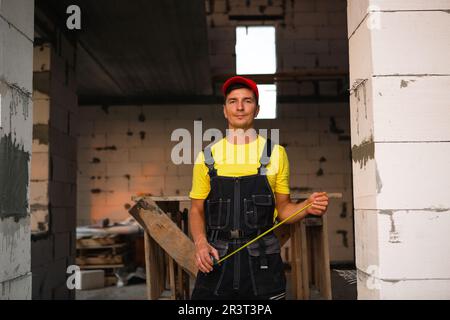 Bauingenieur auf der Baustelle misst die Länge der Fensteröffnung und der Ziegelwand mit einem Maßband. Mann ist drin Stockfoto