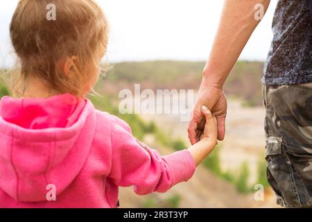 Tochter in einem rosafarbenen Hoodie, die Dads Hand hält und auf einem Berg mit einem wunderschönen Panoramablick steht. Familien-Camping, raus Stockfoto