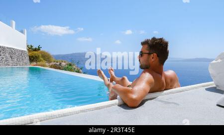 Junger Mann, der sich während des Urlaubs im Santorini Infinity im Swimmingpool mit Blick auf den Ozean erholte Stockfoto