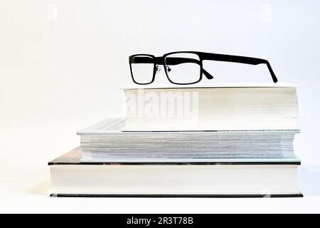 Drei dicke Bücher auf einem Tisch mit Brille als visuelle Hilfe und weißem Hintergrund Stockfoto