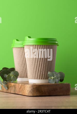 Papierbraune Tassen mit grünem Kunststoffdeckel für Kaffee und Tee auf grünem Hintergrund Stockfoto