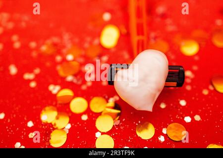 Rasierer mit herzförmigem Rasierschaum. Hellroter Hintergrund mit silbernen Glitzereffekten und goldenen runden Konfetti. Stockfoto