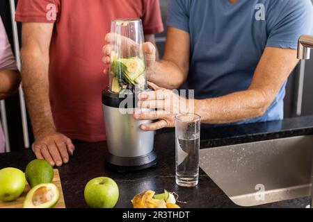 Mittelteil von erfahrenen weißen männlichen Freunden, die zusammen gesunde Smoothies in der Küche zubereiten Stockfoto