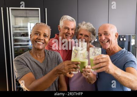 Portrait von glücklichen, vielfältigen Senior-Freunden, die einen Toast mit gesunden Smoothies in der Küche machen Stockfoto
