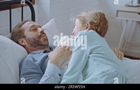 Die Tochter wacht den Vater morgens im Bett auf. Stockfoto