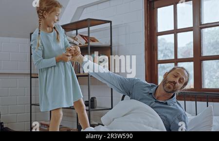 Die Tochter wacht den Vater morgens im Bett auf. Stockfoto