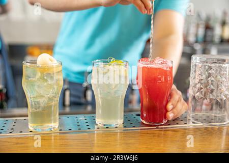 Drei verschiedene Sommercocktails in Steingläsern am Rand einer Bar, wobei der Barkeeper nach einem greift Stockfoto