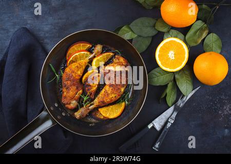 Traditionelle Barbecue-Hähnchenschenkel mit orangefarbenen Scheiben, serviert mit Kräutern als Draufsicht auf einer rustikalen Bratpfanne aus Metall Stockfoto