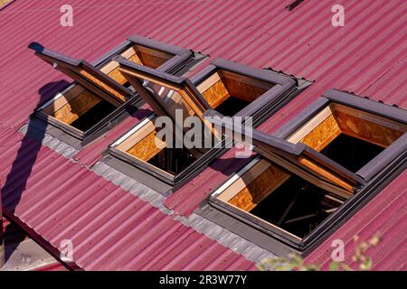 Geöffnete Dachfenster. Dachfenster auf roten Keramikfliesen. Dachfenster, Sonnentunnel. Gebäudekonstruktion, Installation von Metall-Kunststoff-Strukturen Stockfoto