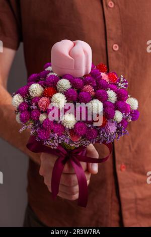 Heiratsantrag. Eleganter Mann in braunem Hemd verleiht einen weißen goldenen Ring in einer rosa Schachtel auf einem wunderschönen Blumenstrauß. Der Kerl hat seiner Freundin einen Heiratsantrag gemacht. Stockfoto