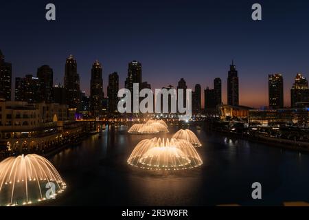 Dubai singende Brunnen bei Nacht Seeblick zwischen Wolkenkratzern. Moderne Architektur in der Dämmerung der Skyline der Stadt in der Innenstadt der Vereinigten Arabischen Emirate Stockfoto