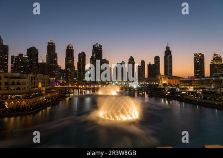 Dubai singende Brunnen bei Nacht Seeblick zwischen Wolkenkratzern. Moderne Architektur in der Dämmerung der Skyline der Stadt in der Innenstadt der Vereinigten Arabischen Emirate Stockfoto