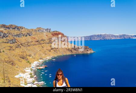 Touristenfrau vor Therasia Hafen, Korfos Strand, Yachthafen und Tavernen am Strand. Auch bekannt als Thirasía .Kykladen, Griechenland Stockfoto