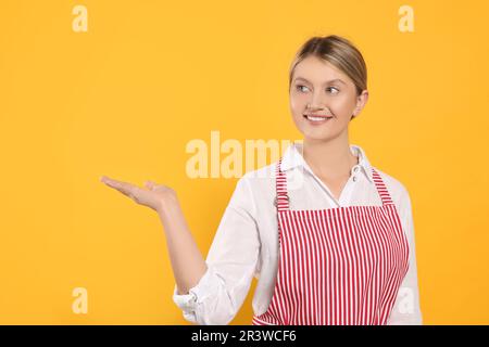 Wunderschöne junge Frau in einer sauberen gestreiften Schürze auf orangefarbenem Hintergrund Stockfoto