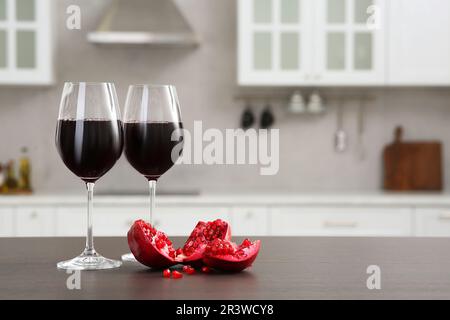 Gläser Rotwein und frische Granatäpfel auf der Arbeitsfläche in der Küche, Platz für Text Stockfoto