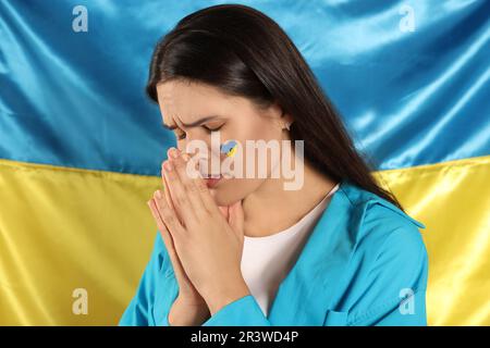 Traurige junge Frau mit gefalteten Händen nahe der ukrainischen Flagge Stockfoto